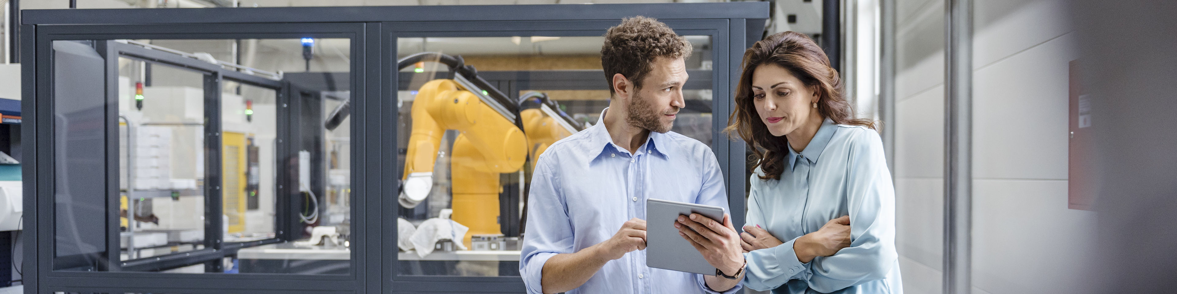 Colleagues in high tech company controlling industrial robots, using digital tablet