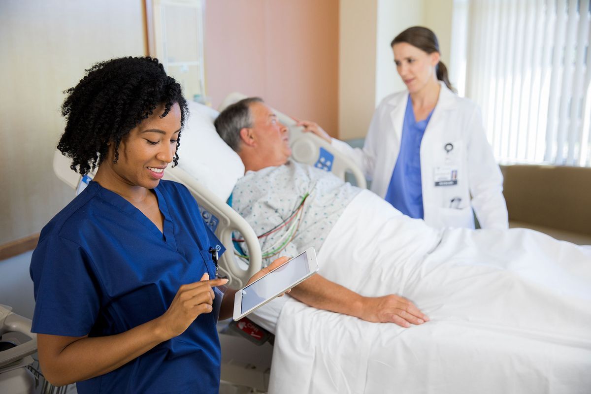 Nurse checking tablet screen with patient and doctor in background