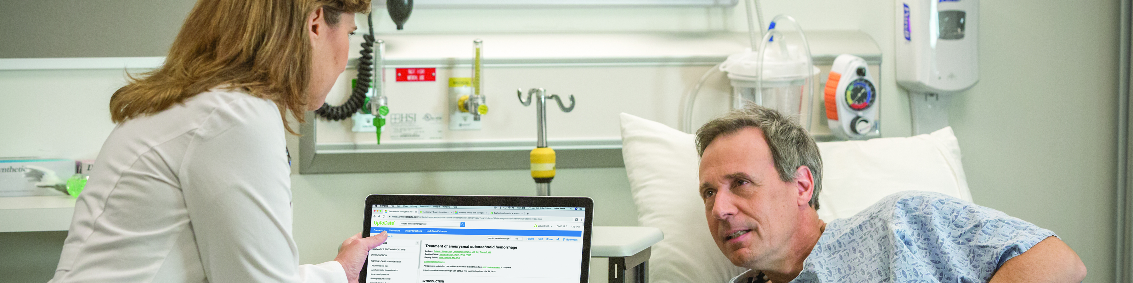 Doctor and patient in hospital room, doctor using UpToDate on computer