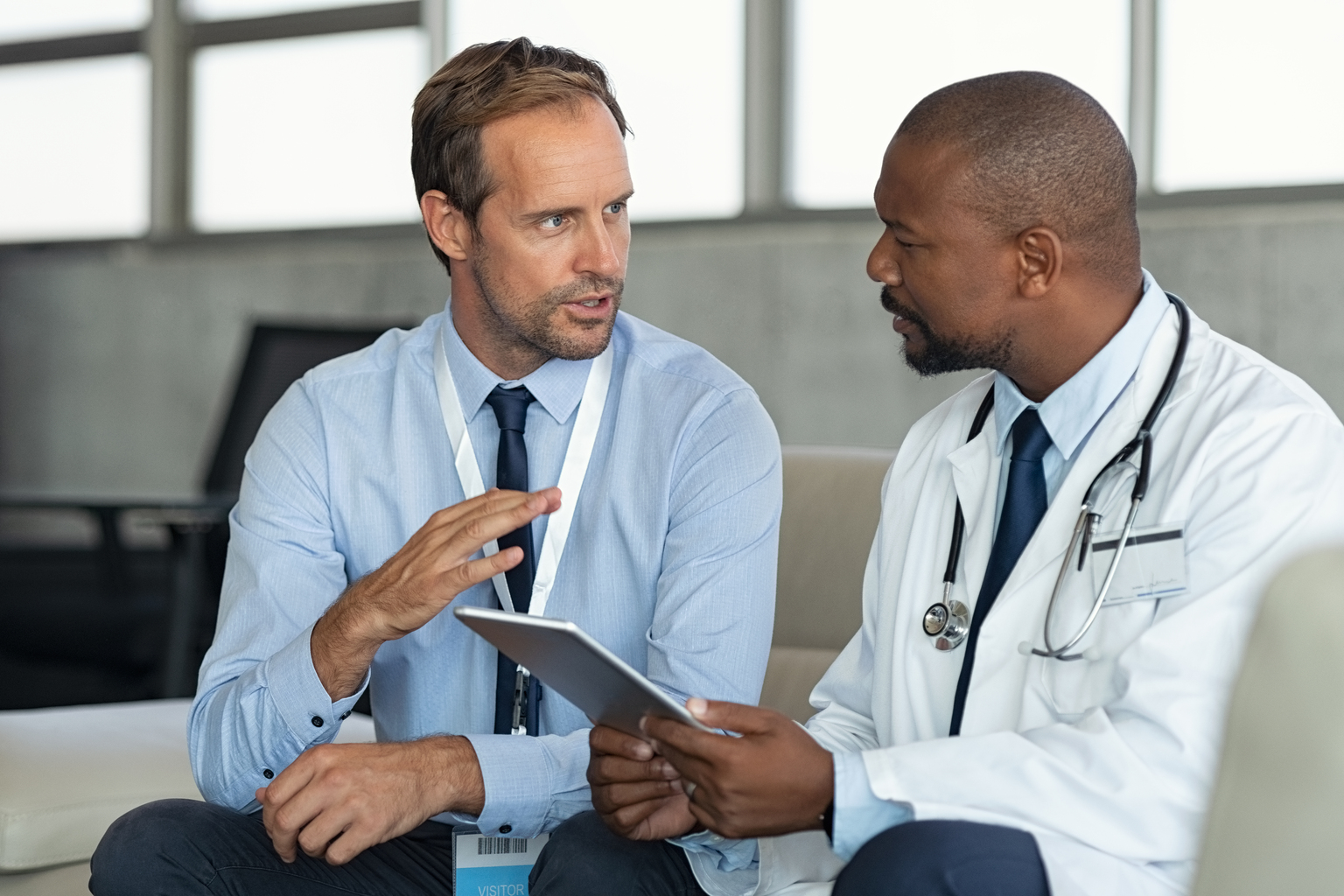 African male doctor talks with white male pharmaceutical representative.