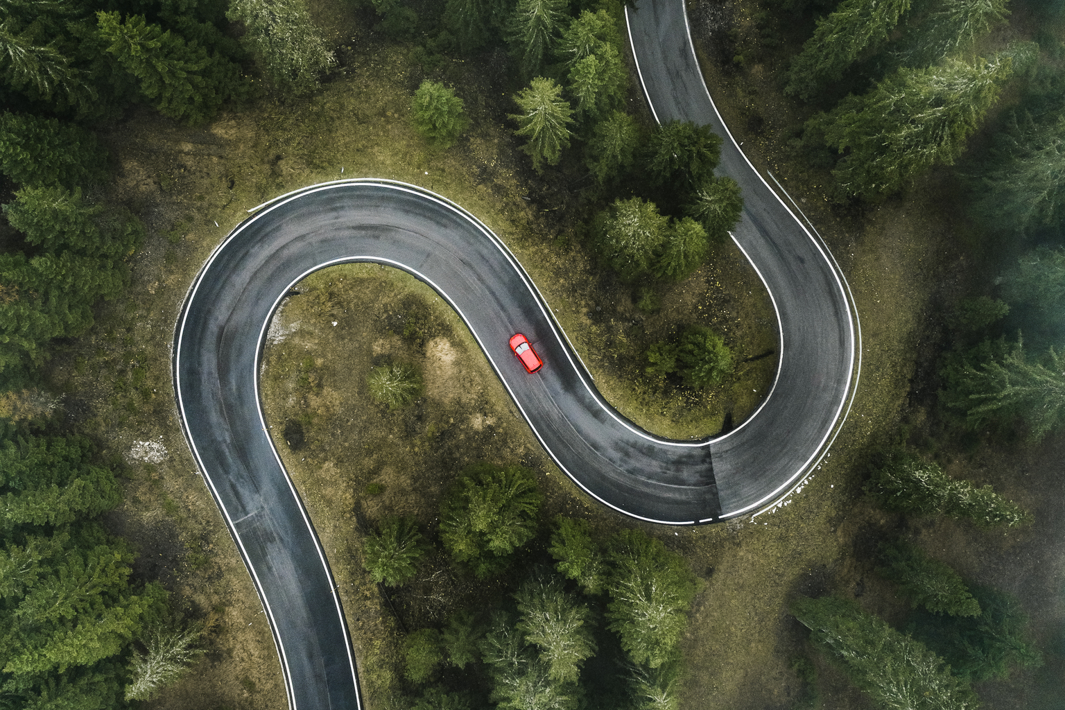 A car driving on a winding forest road seen from directly above, Dolomites, Italy,