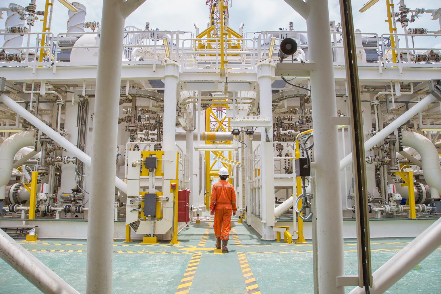 Technician walking through offshore oil and gas process for checking the condition of equipment on platform.