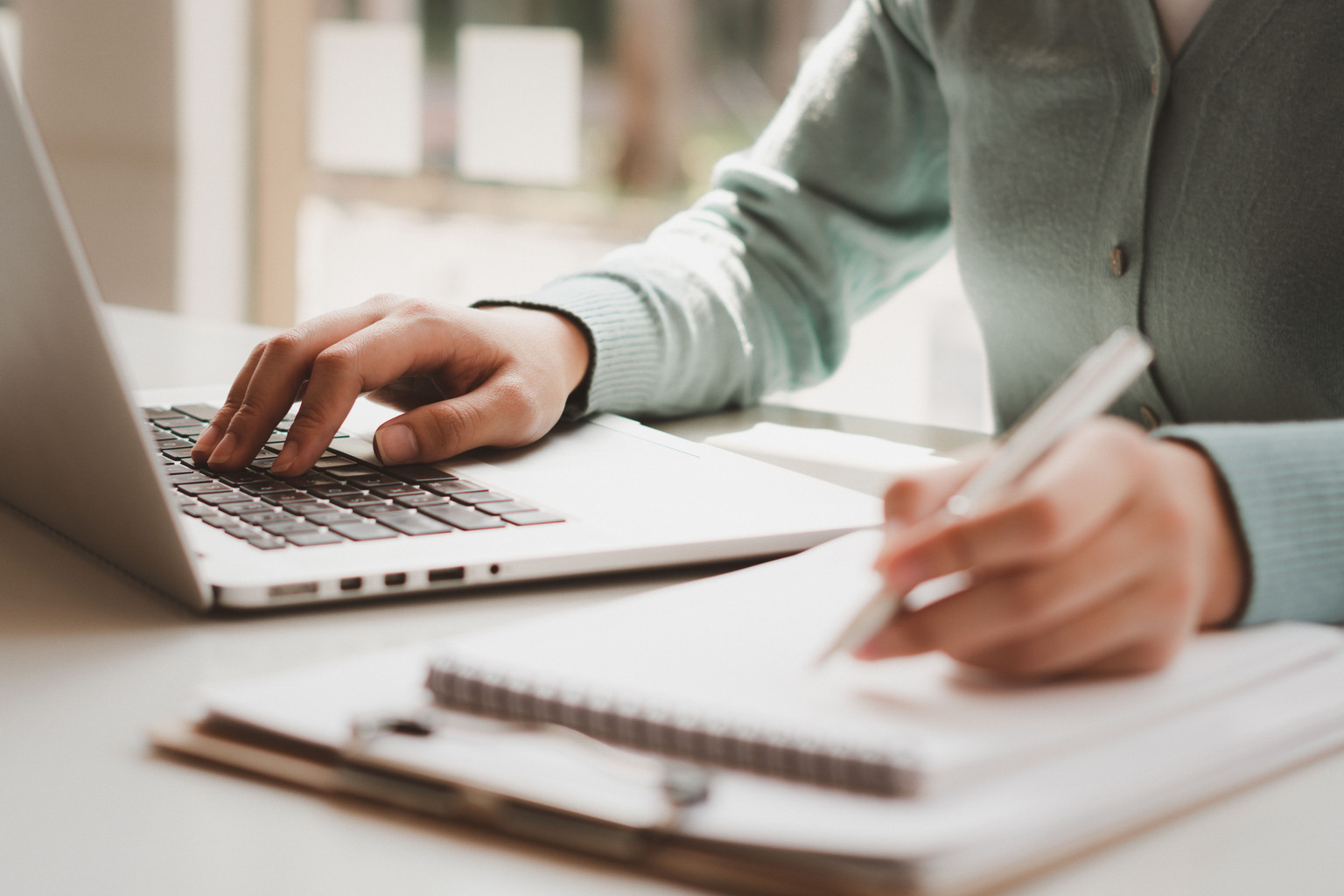 Business women work on computers and write on notepad with pen within the office