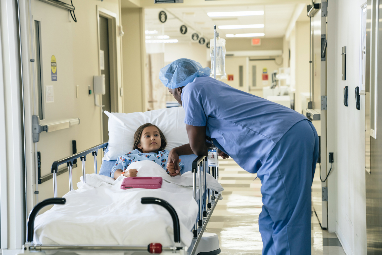 African male doctor holding hand of girl in hospital gurney.