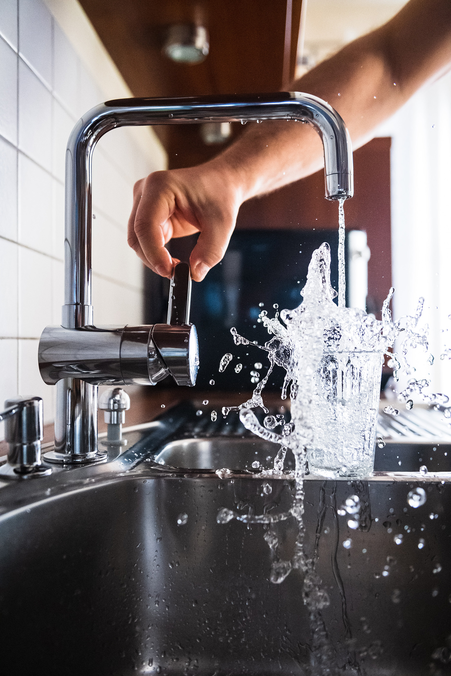 Hand turning on sink faucet water splashing over glass