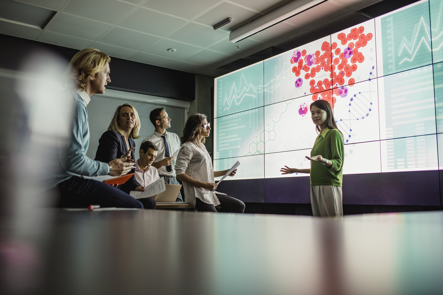 Group of business professionals in a dark room standing in front of a large data display screen with information