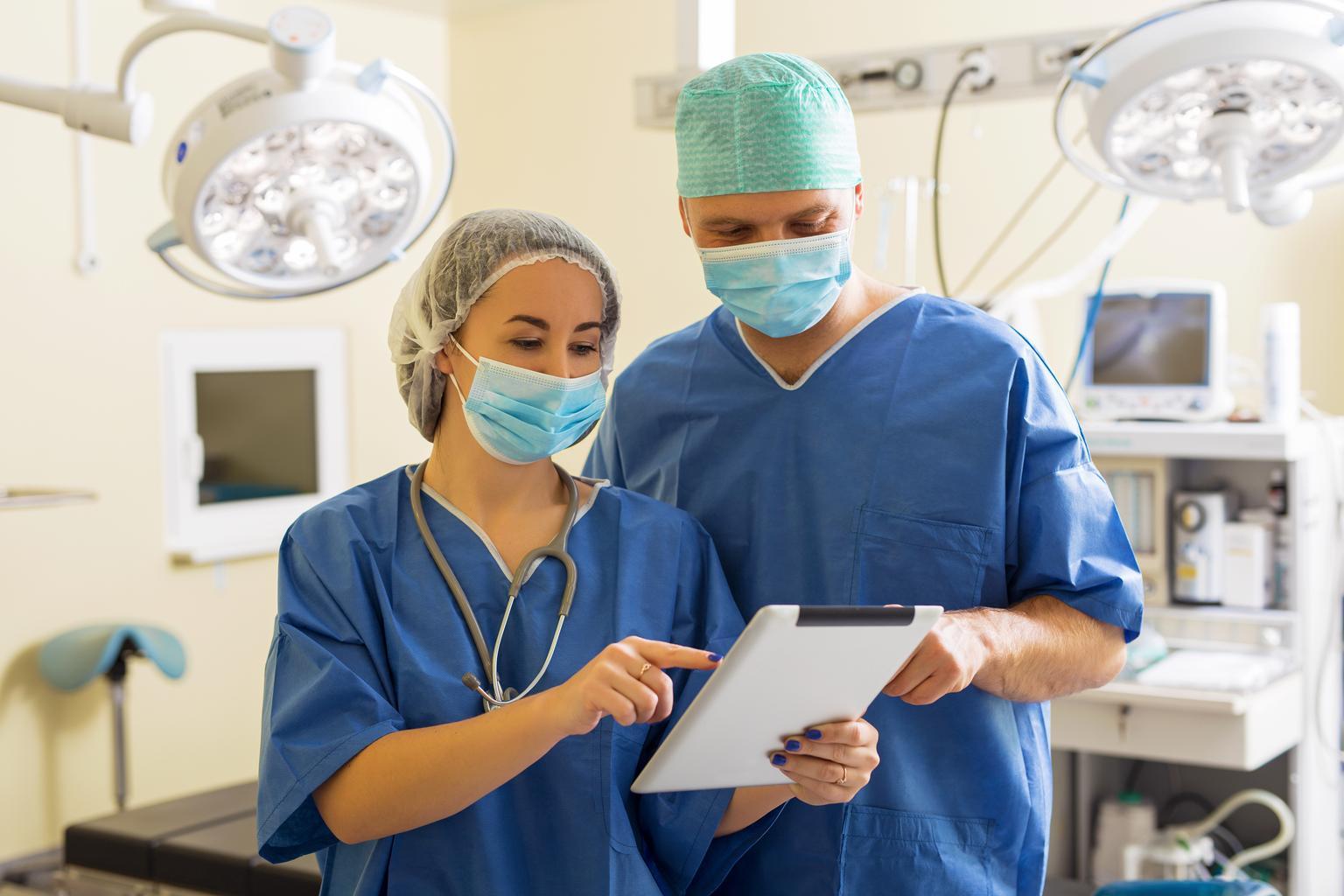 Doctor and assistant looking at tablet in hospital surgery room