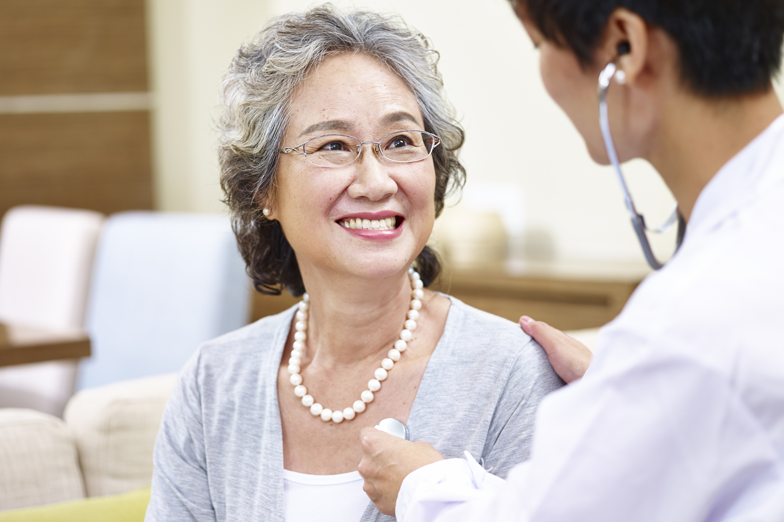 Family doctor checking smiling senior Asian woman using stethoscope