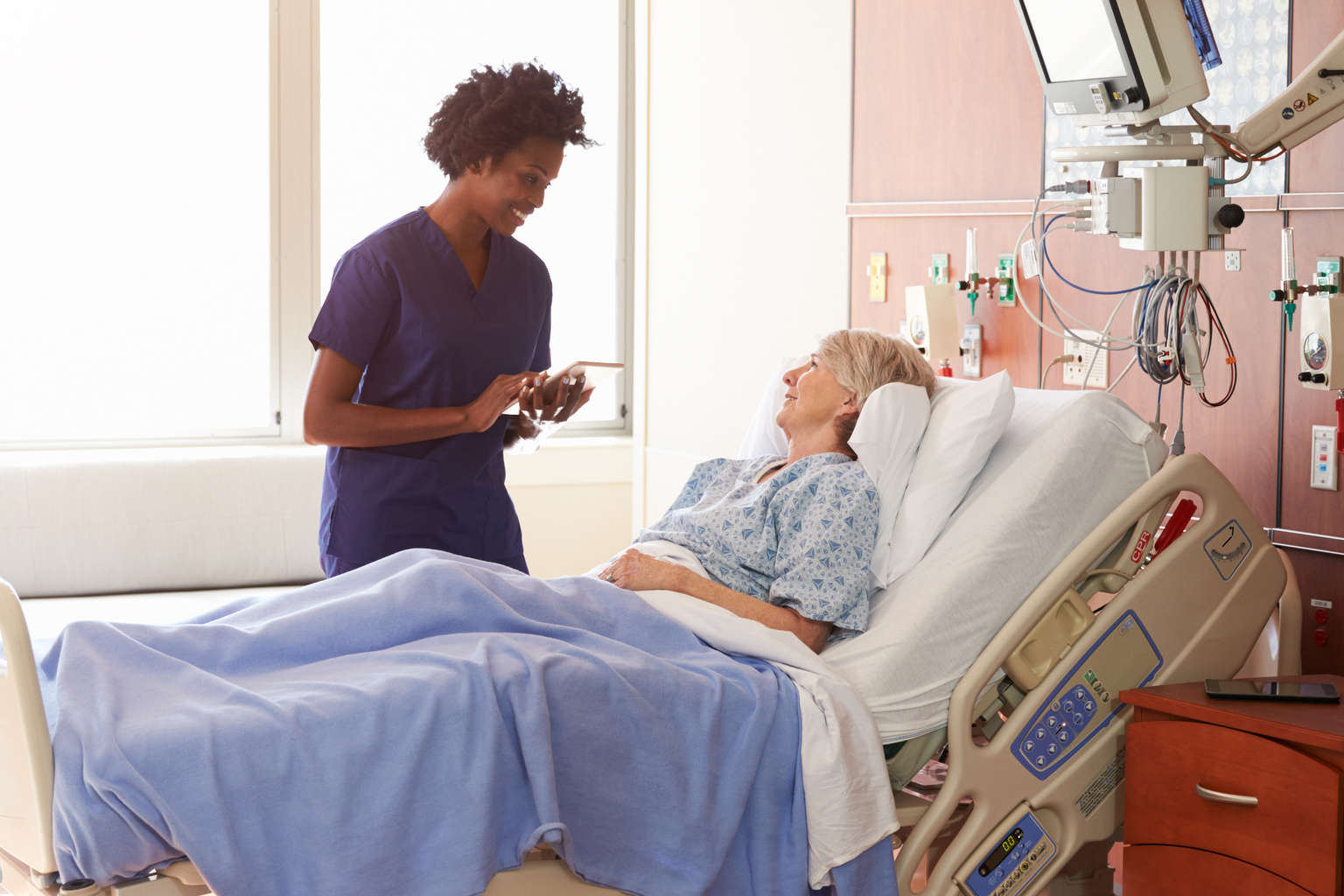 Hospital Nurse With Digital Tablet Talks To Senior Patient