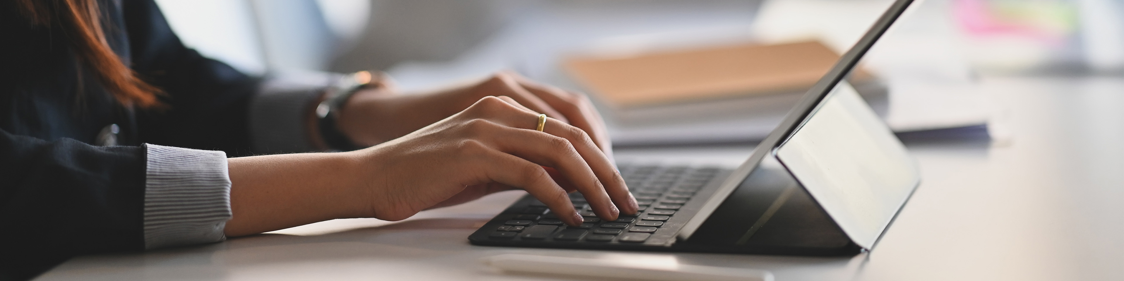 Cropped shot of business woman hand while typing on computer tablet and sitting next to her colleague