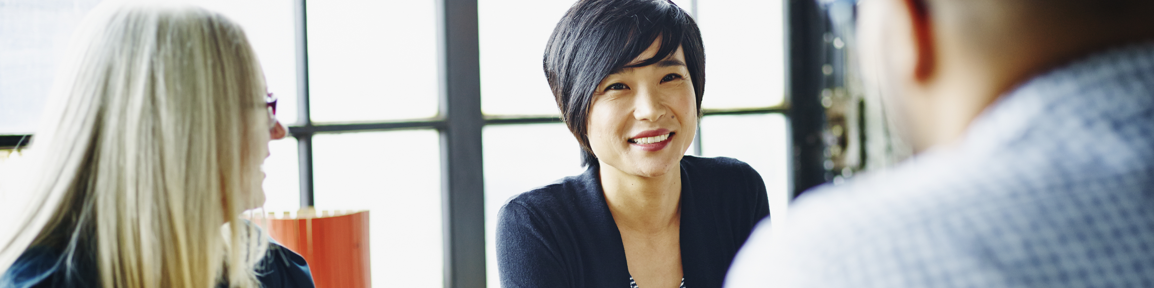 Smiling businesswoman leading discussion with colleagues during meeting at office conference table