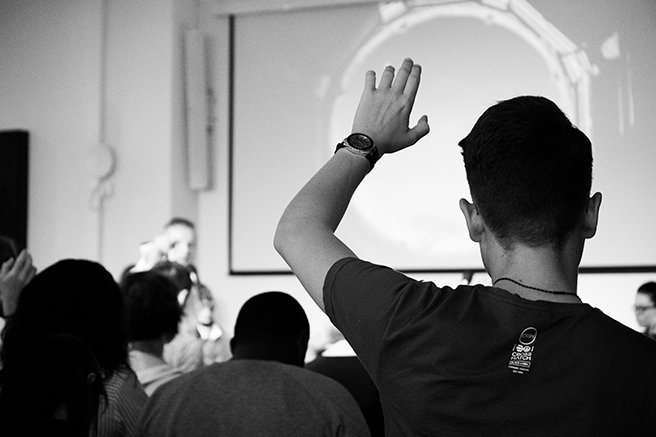 Black and white image of person with their hand raised at a conference presentation