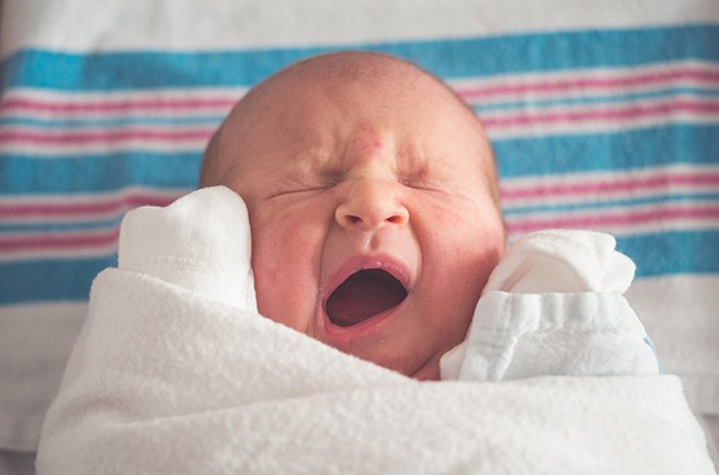 Close up on a swaddled newborn yawning
