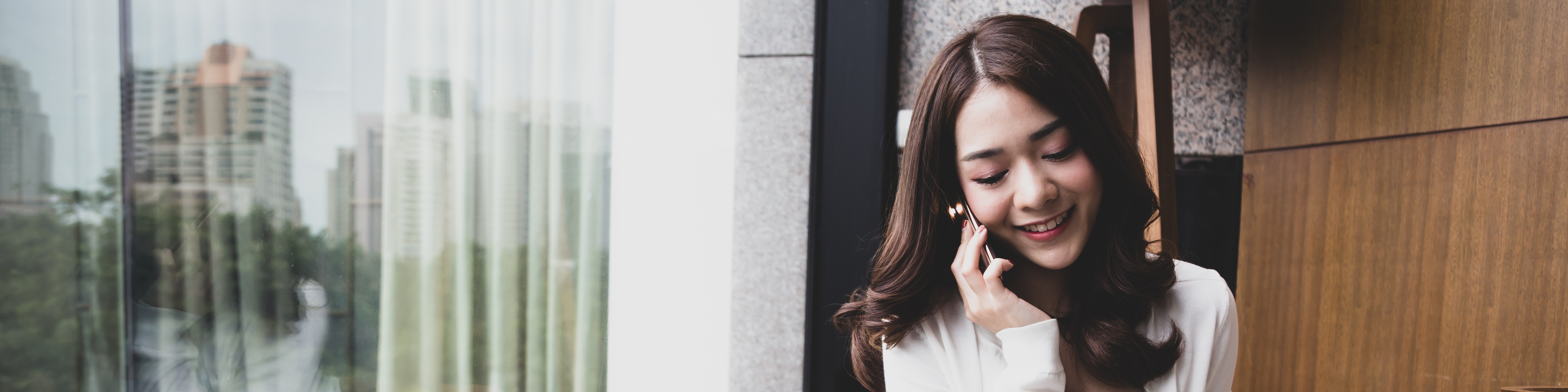 Young Asian woman using phone and laptop with coffee next to window