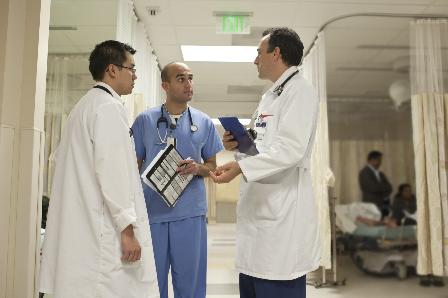 Three male doctors in discussion in emergency room.