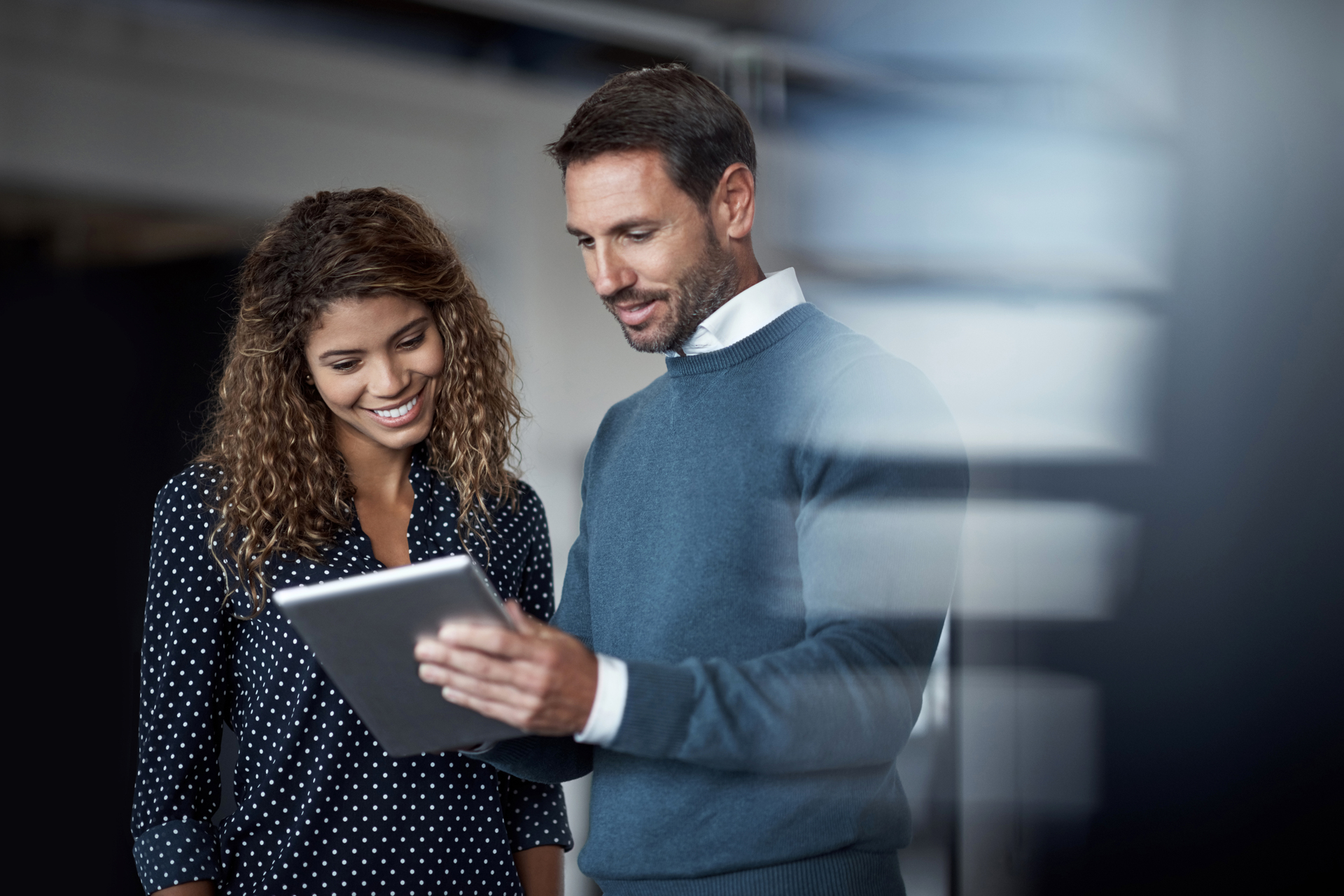 Shot of two colleagues working on a digital tablet together while standing in a large office