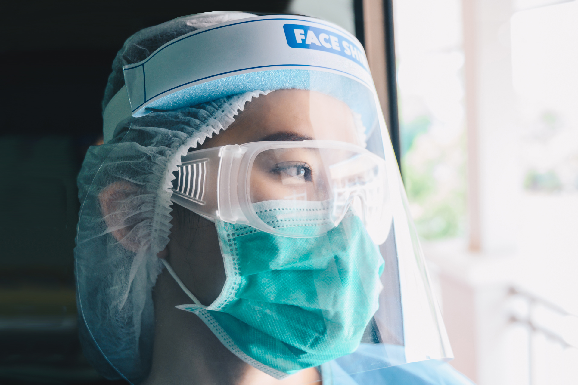 Healthcare working looking out window, wearing full PPE coverage including mask, eye wear, and face shield