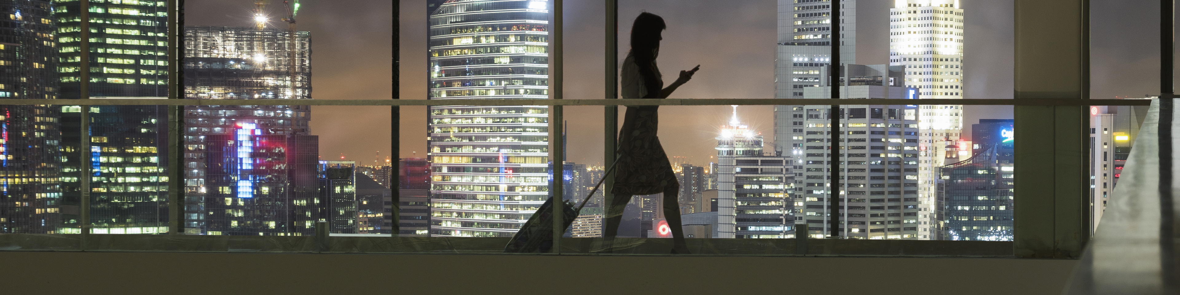 Young woman using smartphone and pulling suitcase, city skyline in view 