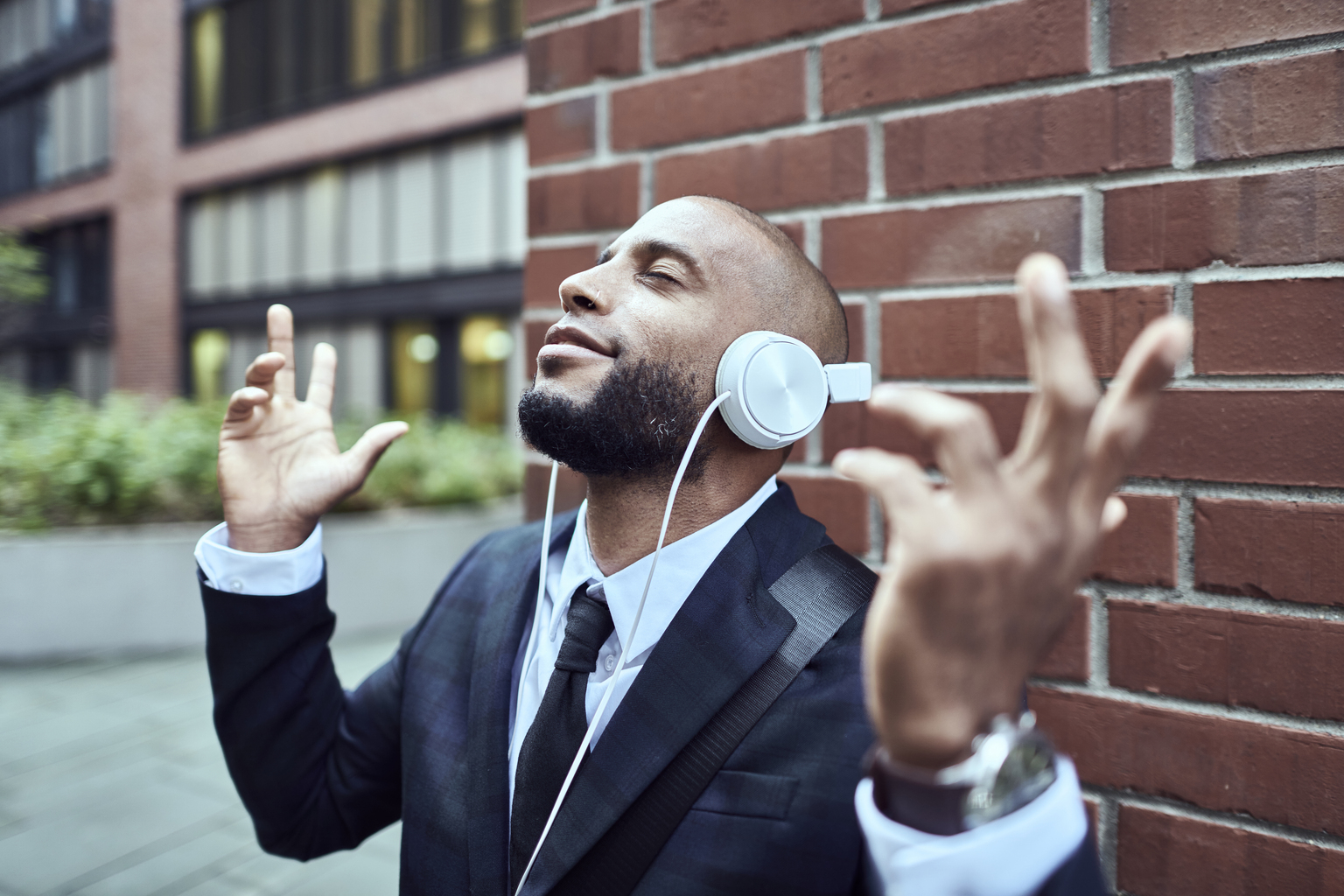 Young fashionable male, listening his favorite song on his wireless headphones,leaning on brick wall