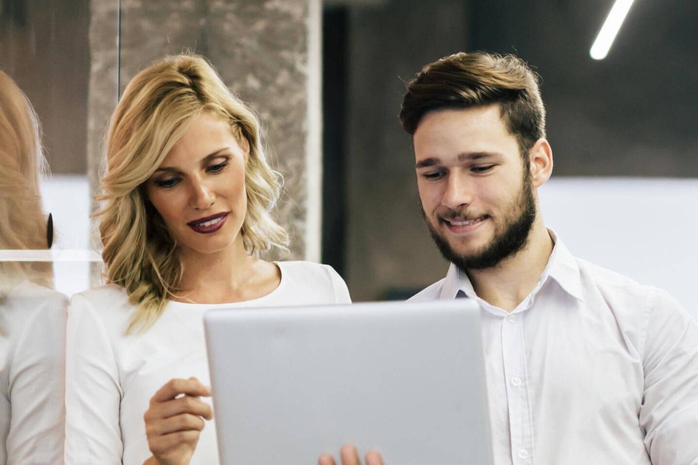 a man and a woman in business casual attire standing and reviewing information on a laptop
