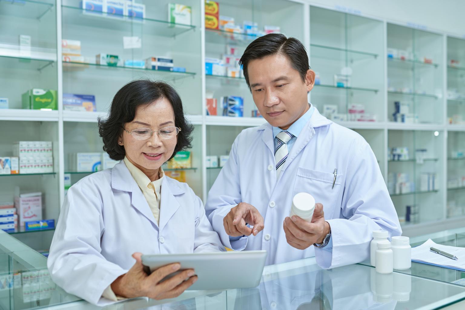Two Asian pharmacists with tablet and pill bottle