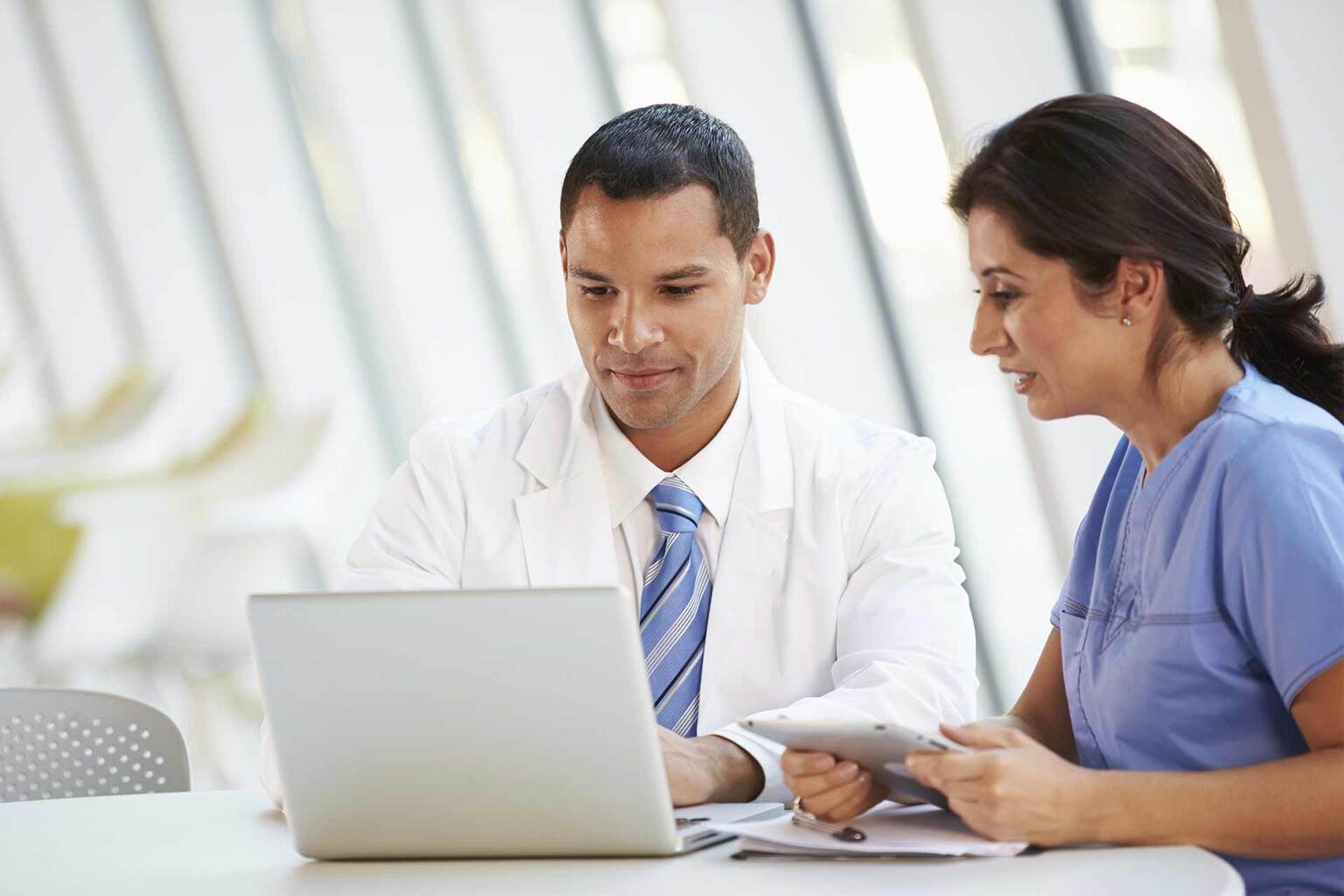 Nurse checking tablet screen with patient and doctor in background