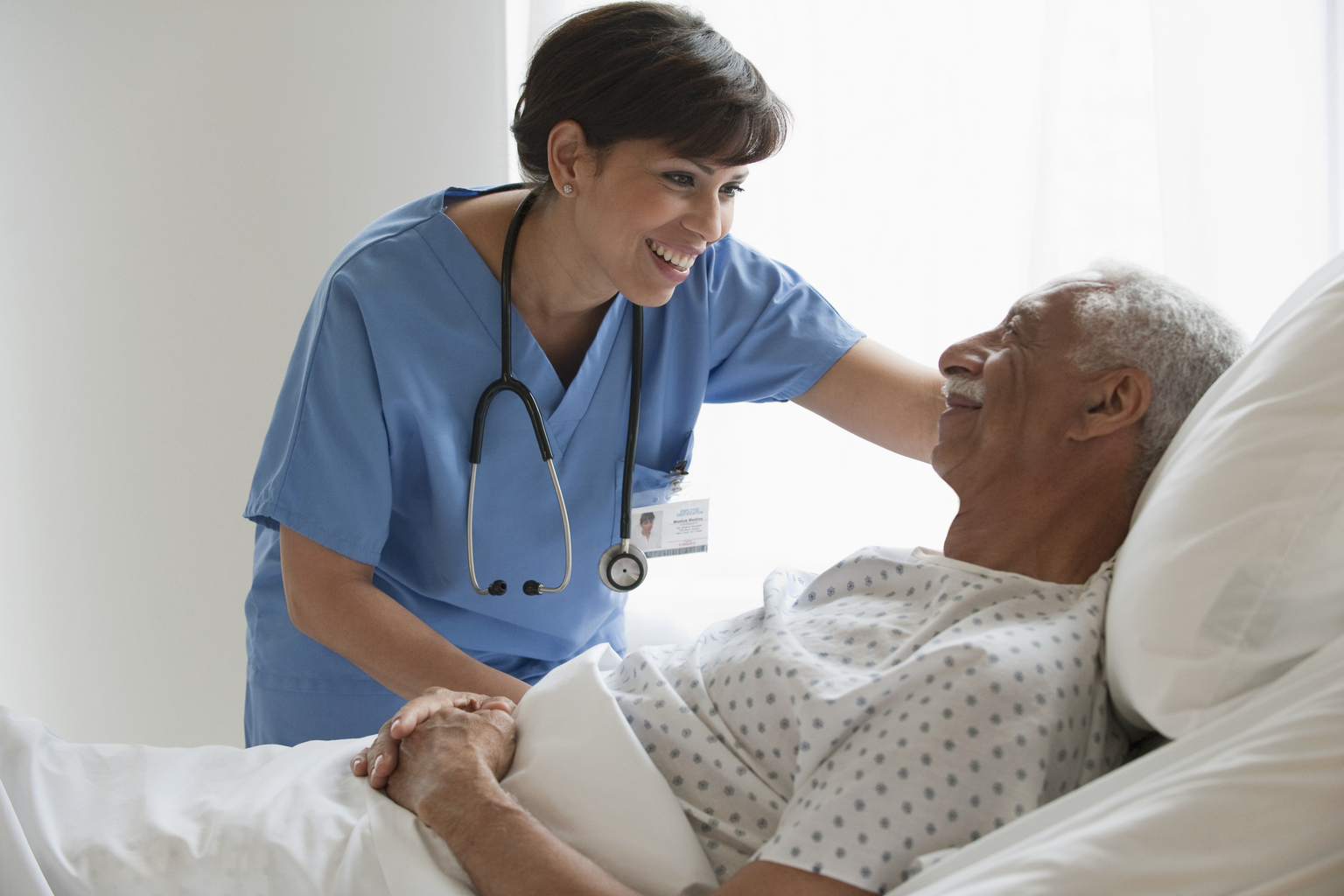 Female nurse cares for senior male patient in hospital bed.