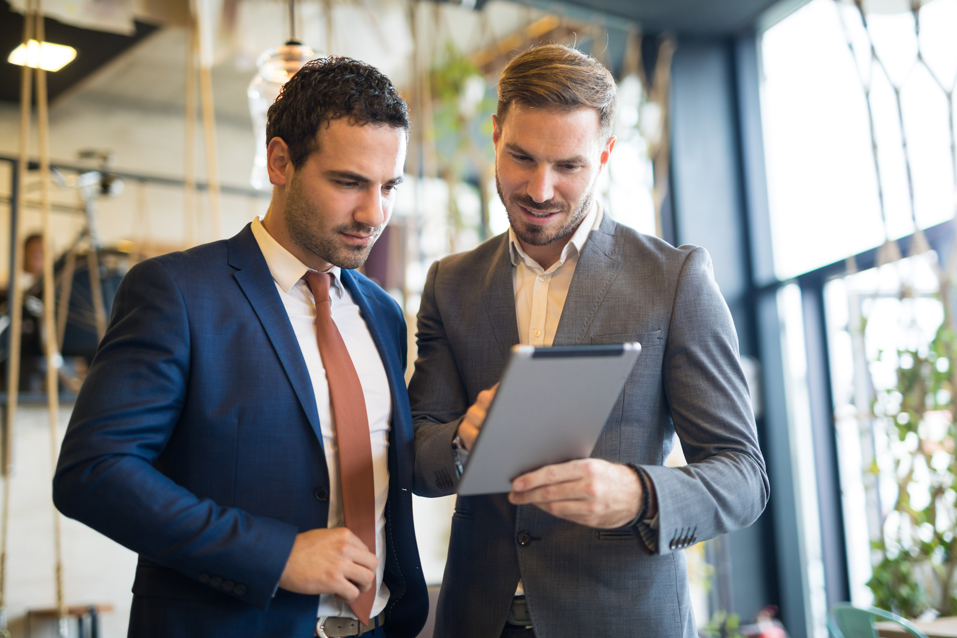 Two young businessmen are discussing business strategy in the office building hallway using digital tablet.