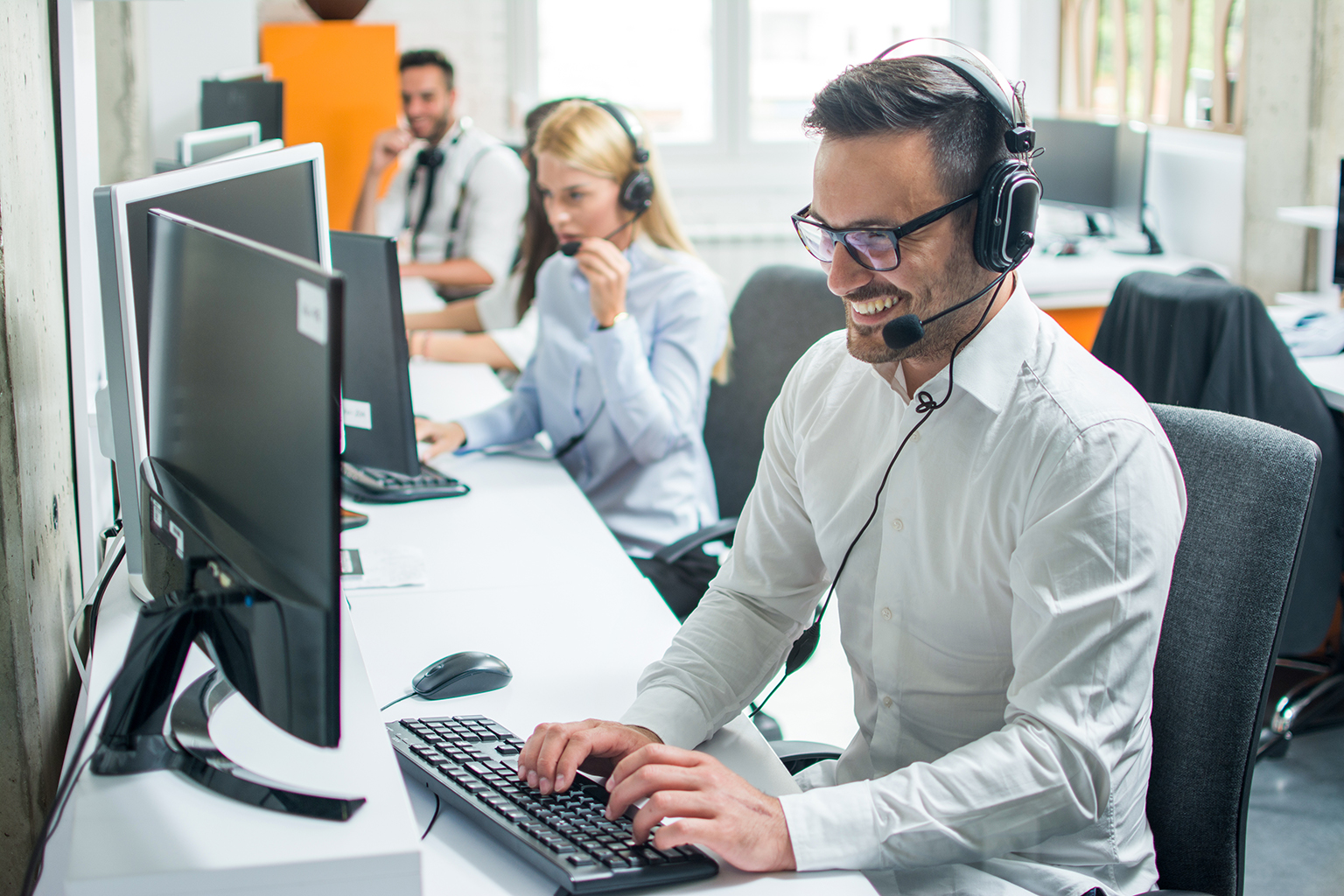 Call center staff working at computers, focus on gentleman in front on headset