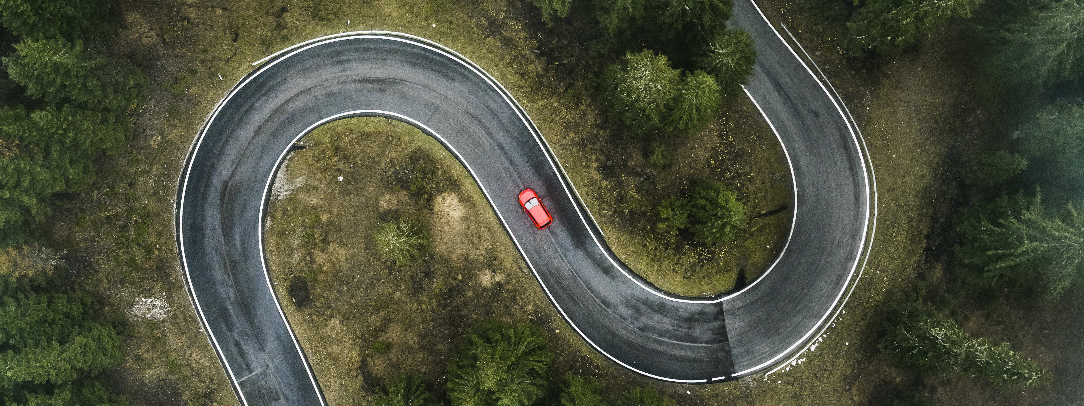 A car driving on a winding forest road seen from directly above, Dolomites, Italy,