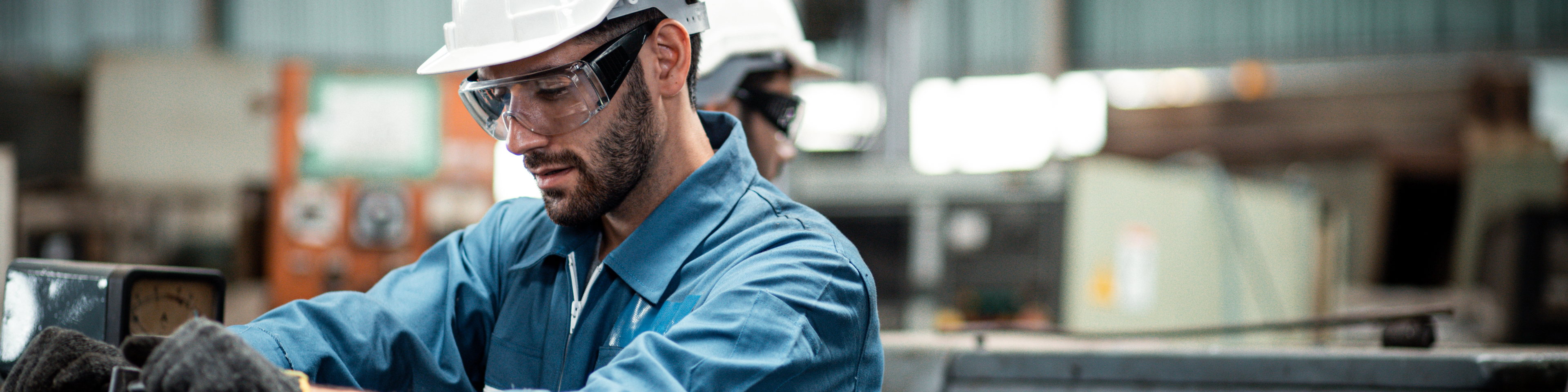 Men industrial engineer wearing a white helmet while standing in a heavy industrial factory behind. The Maintenance looking of working at industrial machinery and check security system in factory.