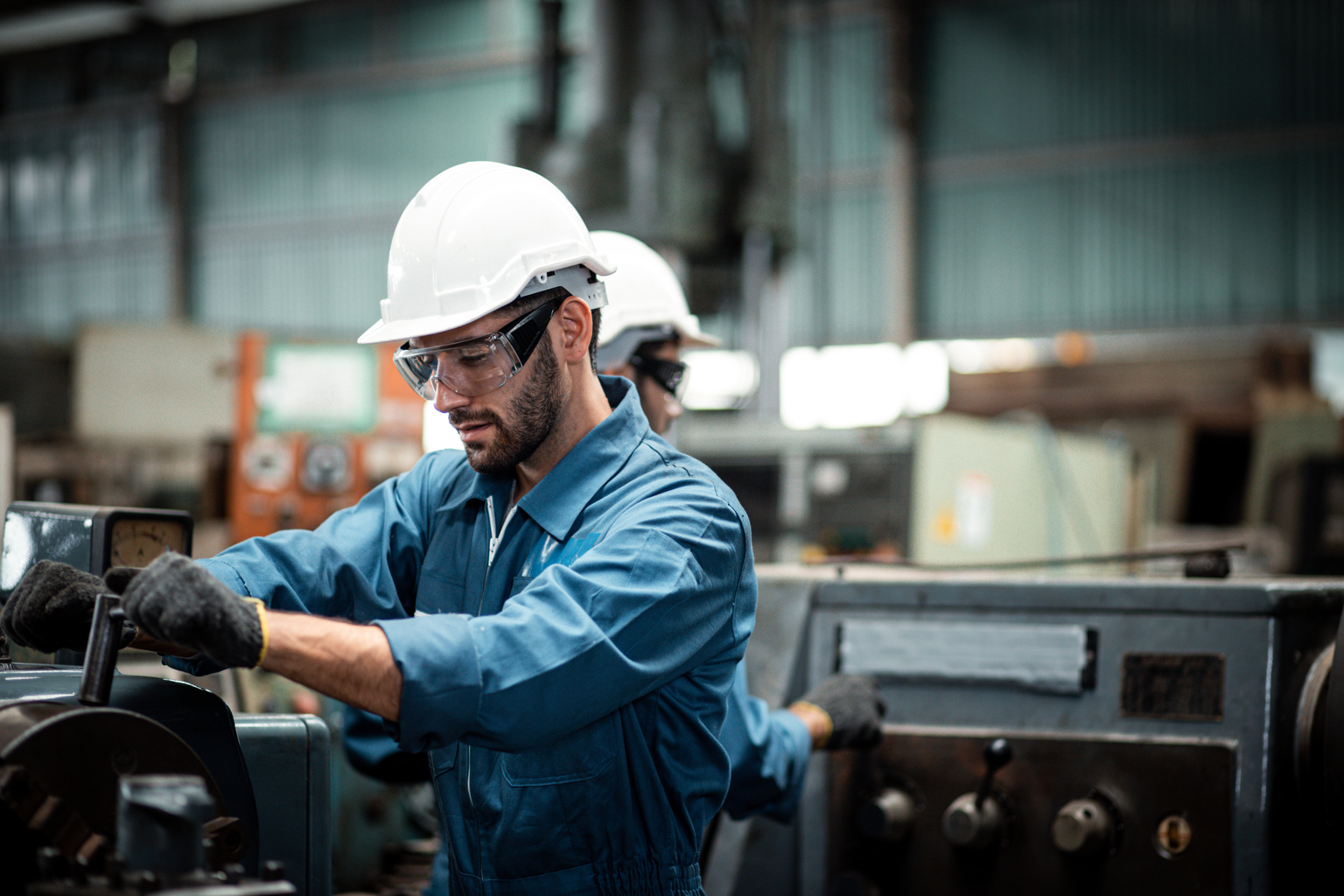 Men industrial engineer wearing a white helmet while standing in a heavy industrial factory behind. The Maintenance looking of working at industrial machinery and check security system in factory.