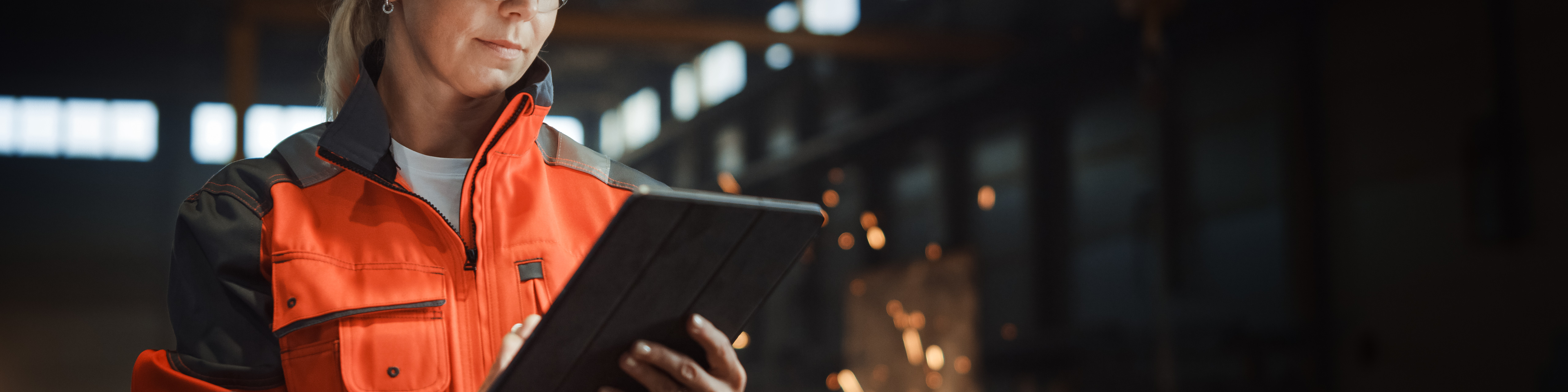Professional Heavy Industry Engineer Worker Wearing Safety Uniform and Hard Hat Uses Tablet Computer. Serious Successful Female Industrial Specialist Standing in a Metal Manufacture Warehouse.