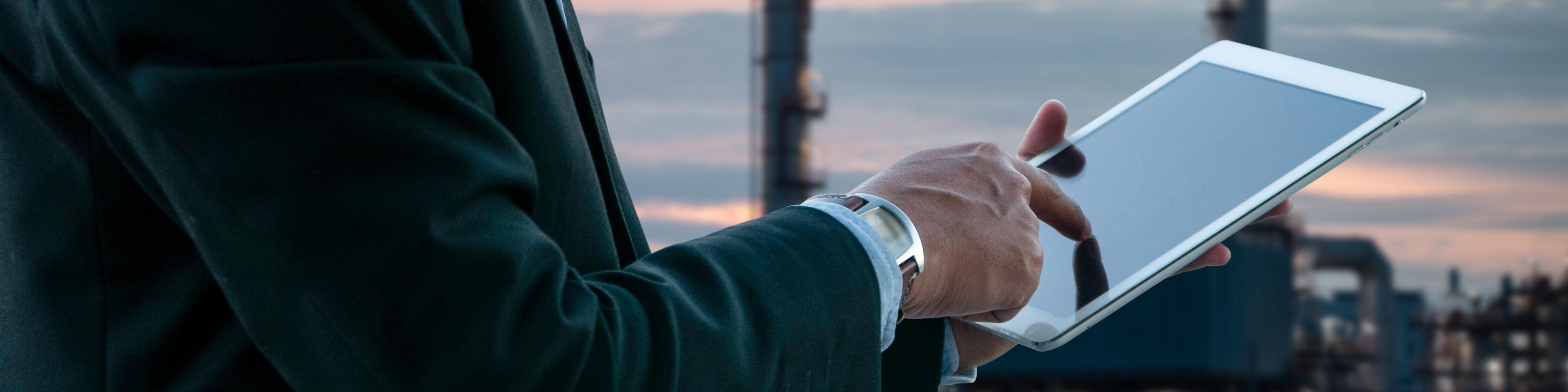 Business man working on media pad with oil and gas refinery background.