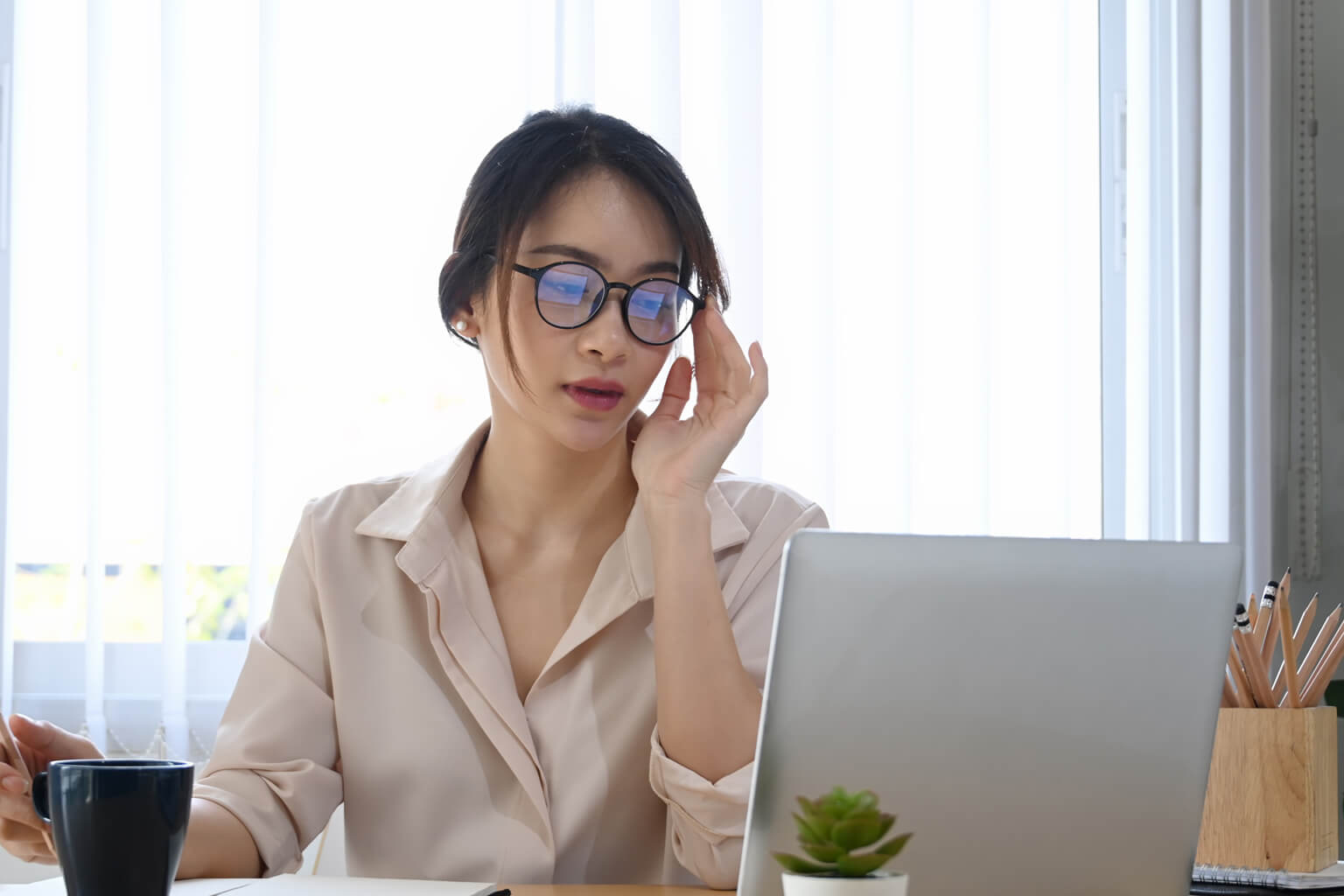 A woman touching her glasses and looking at a laptop