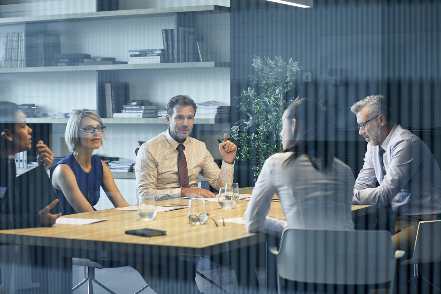 Business people communicating at desk seen through glass. Coworkers are discussing in meeting. They are sitting in office.