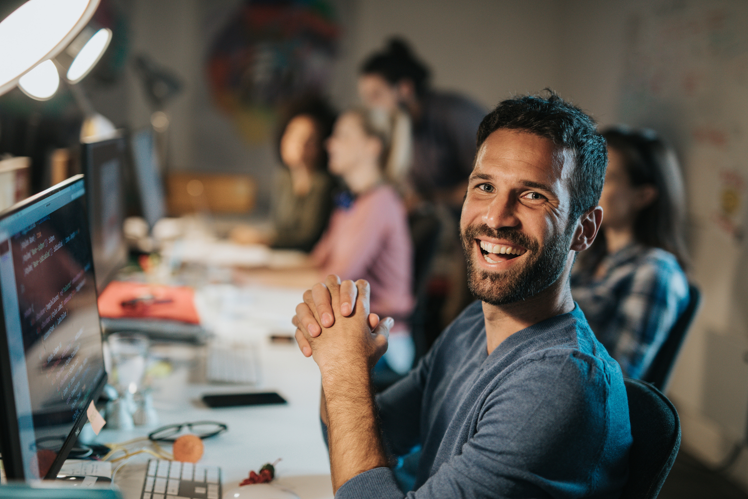 Portrait of a young happy programmer coding data while working on desktop PC in the office