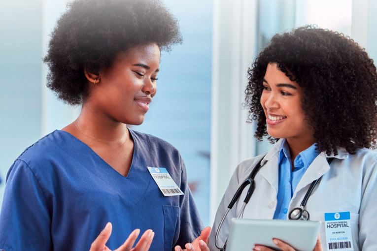 Two medical professionals meeting casually in a hospital wing to review information on a tablet