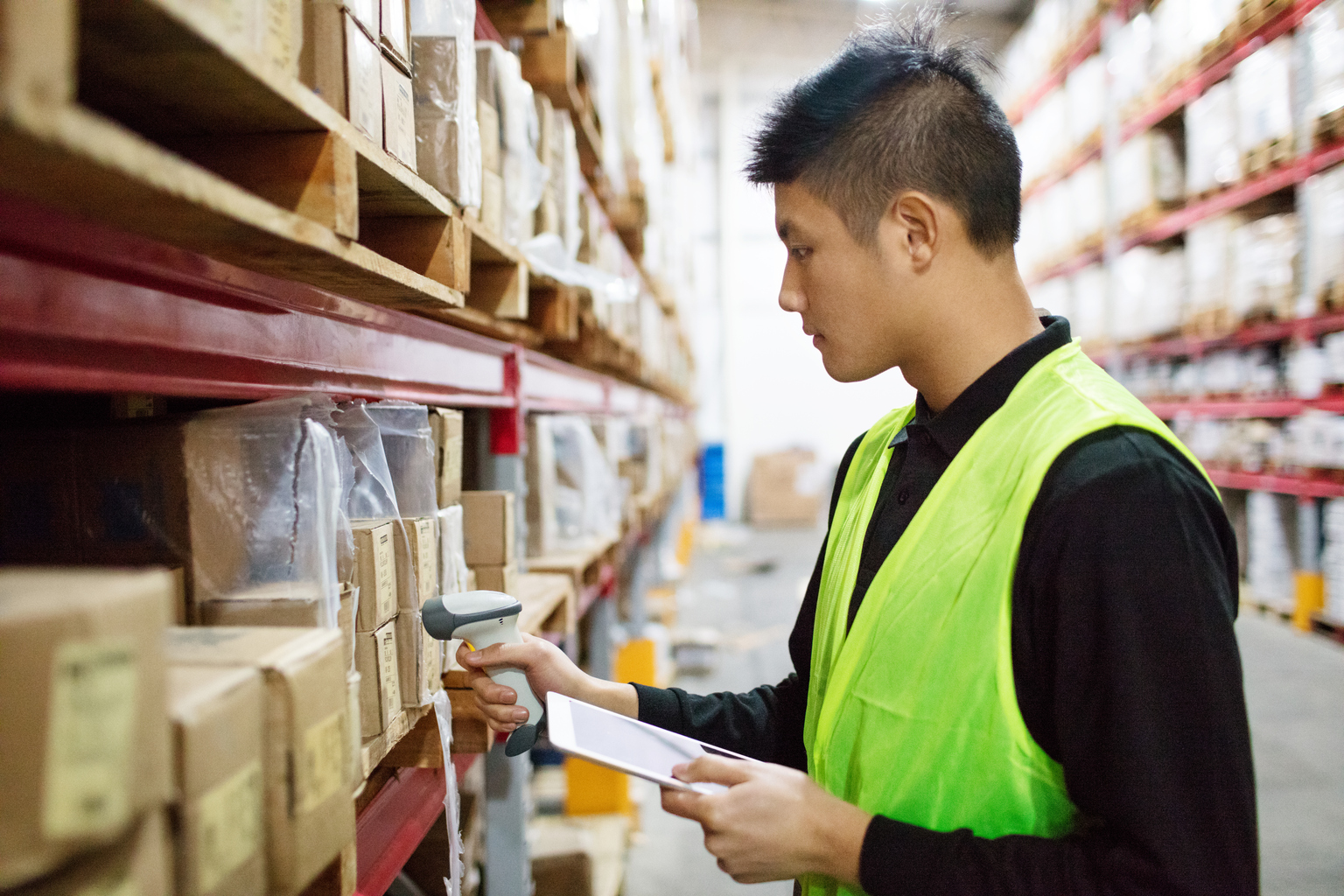Warehouse worker checking cargo on shelves with scanner. Male worker in uniform holding digital tablet and scanning boxes in shelves