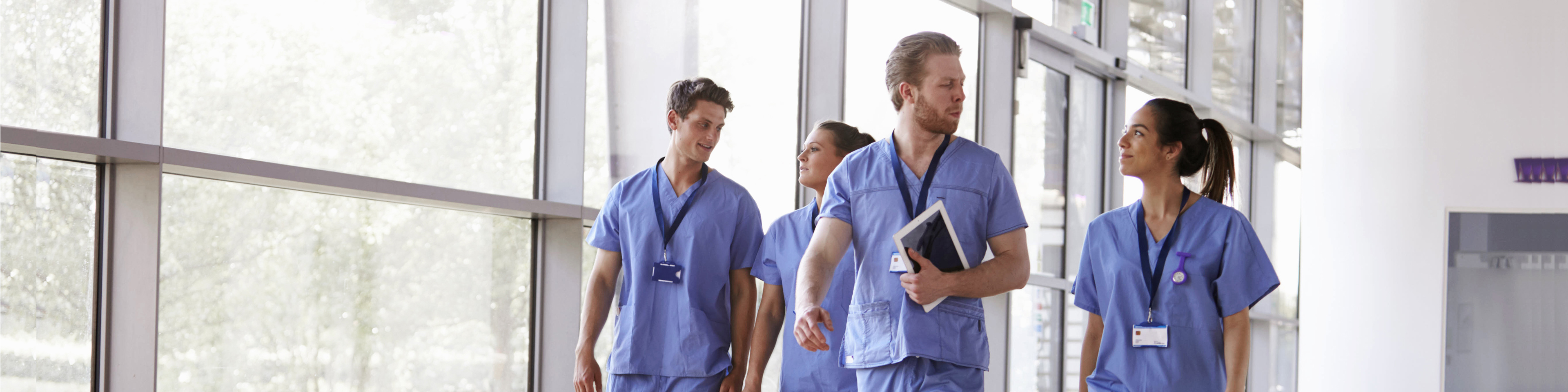 Four healthcare workers in scrubs walking in corridor