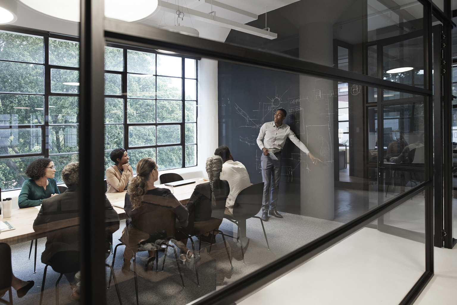 Businessman explaining while male and female colleagues sitting in conference room seen through glass wall at workplace.