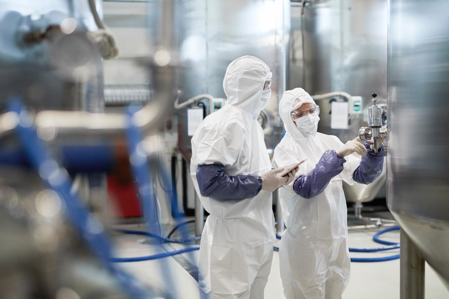 Side view portrait of two workers wearing protective suits while using equipment at modern chemical plant, copy space