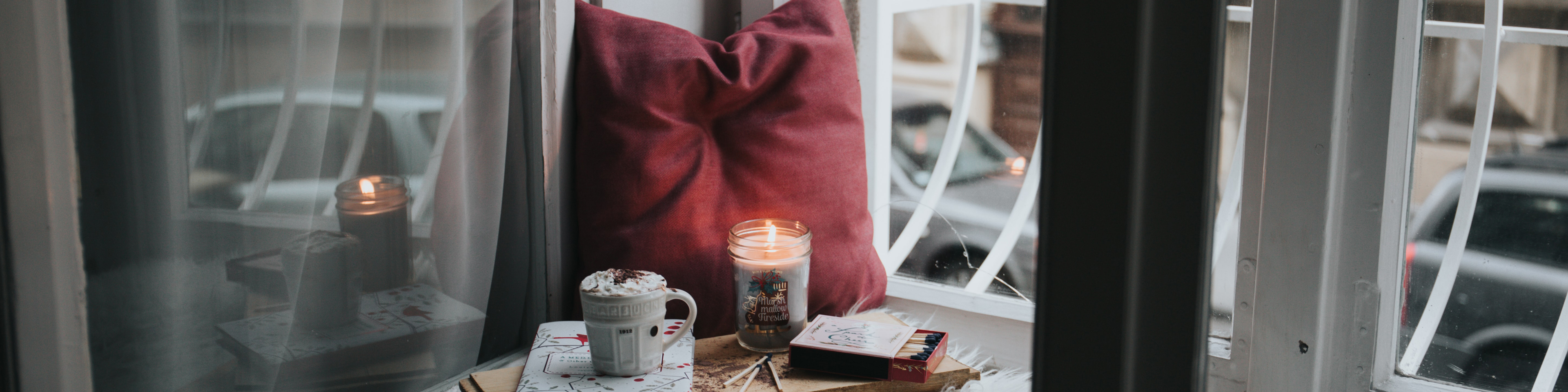 Window seat with blanket, pillow, book, drink, and candle