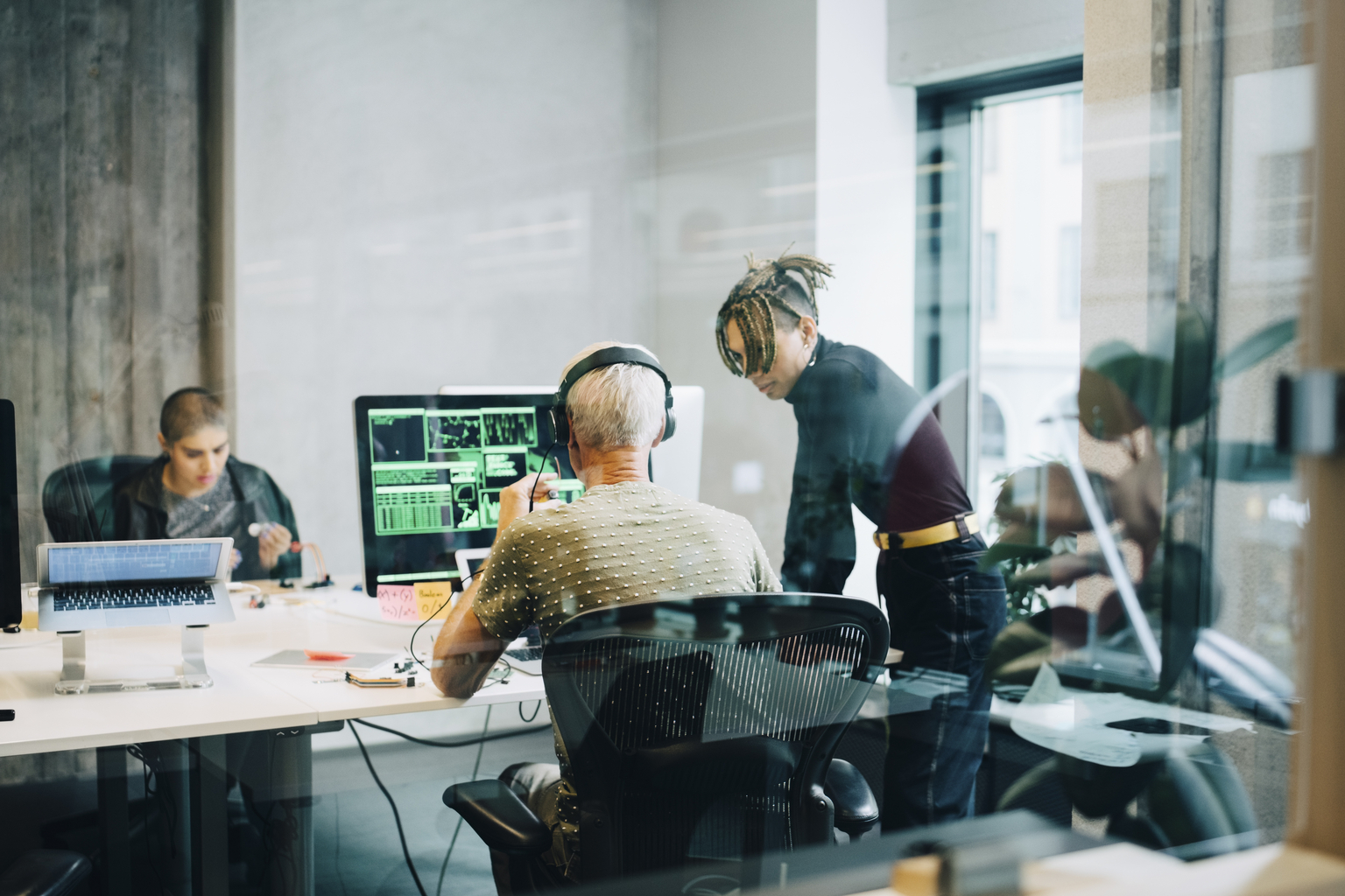 Male Engineer discussing with colleague while coding over computer at office