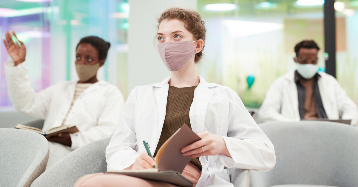 Female med student taking notes, additional students out of focus in background