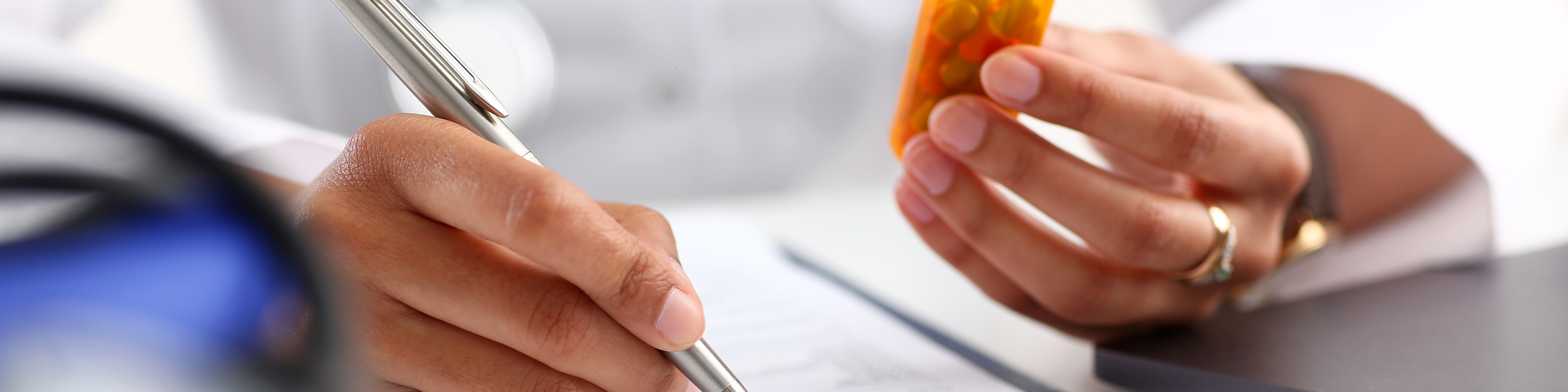 Close up on doctor writing on clipboard while holding a prescription bottle of pills