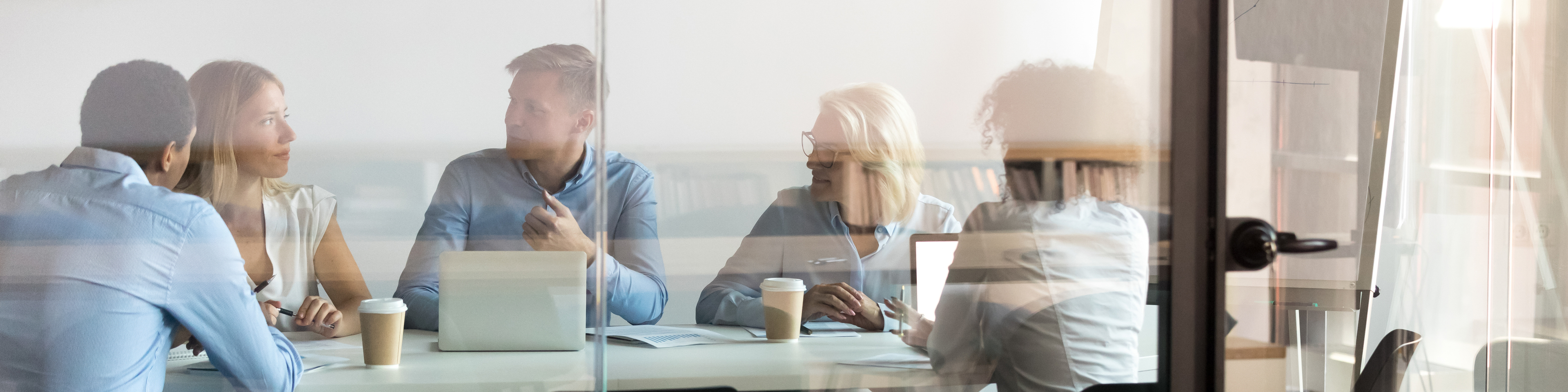 Advertising department brainstorming at modern office boardroom behind closed doors, view through the glass wall. Diverse staff led by ceo discussing new project sharing ideas thoughts and sales pitch