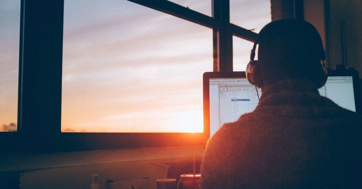 man werkt op laptop met hoofdtelefoon met zicht op zonsondergang