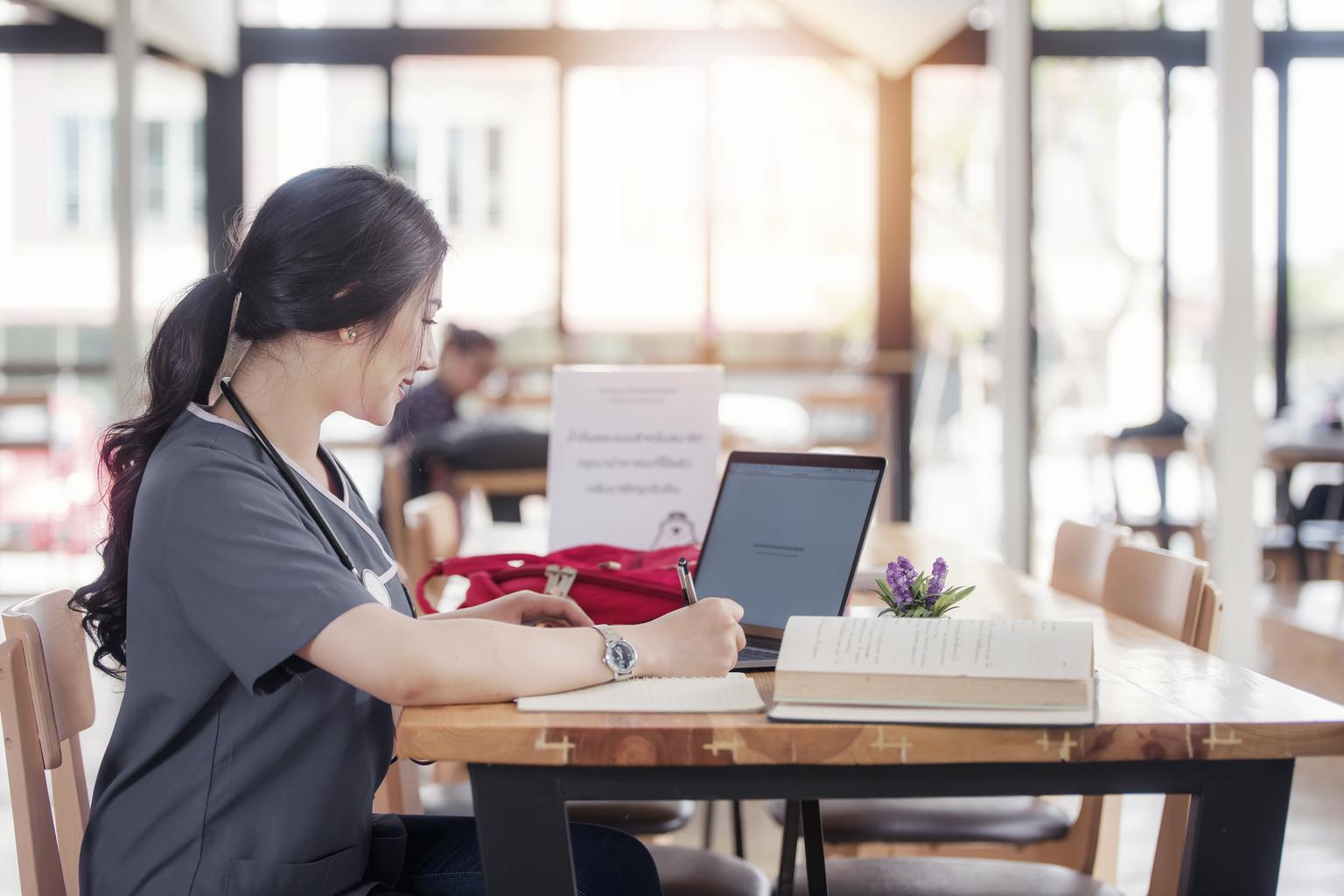 Nursing student wearing grey scrubs studies in sunny library