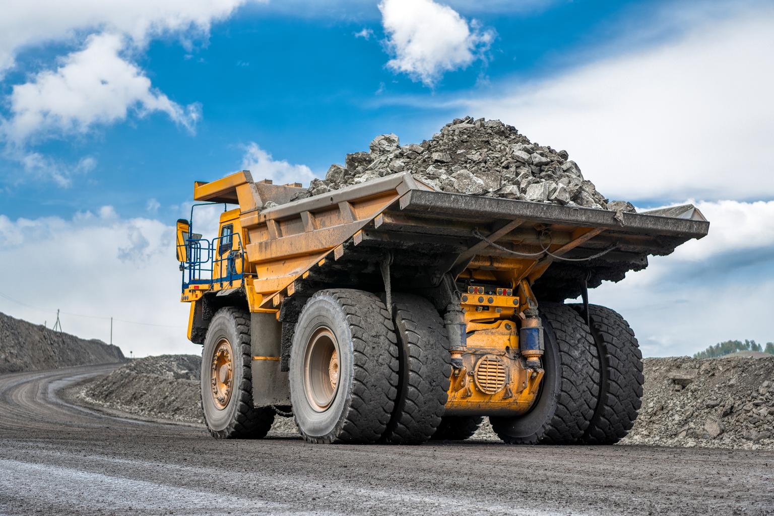 Rock transportation by dump trucks. Large quarry yellow truck. Transport industry. Mining truck is driving along a mountain road.